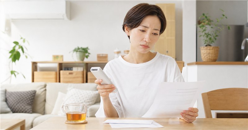 夏のリビングでエアコンのリモコンを操作する女性