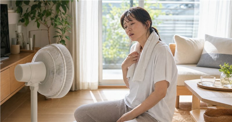 マンション室内で扇風機の前に座る女性・熱中症対策のアイキャッチ